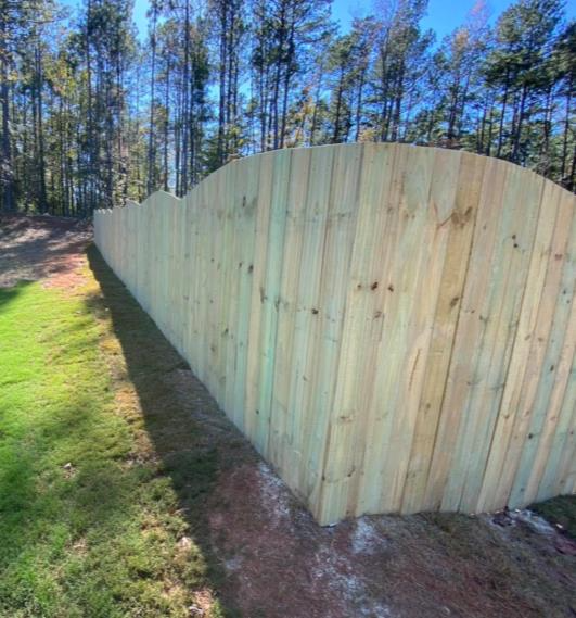 Scalloped privacy fence installed along a tree line
